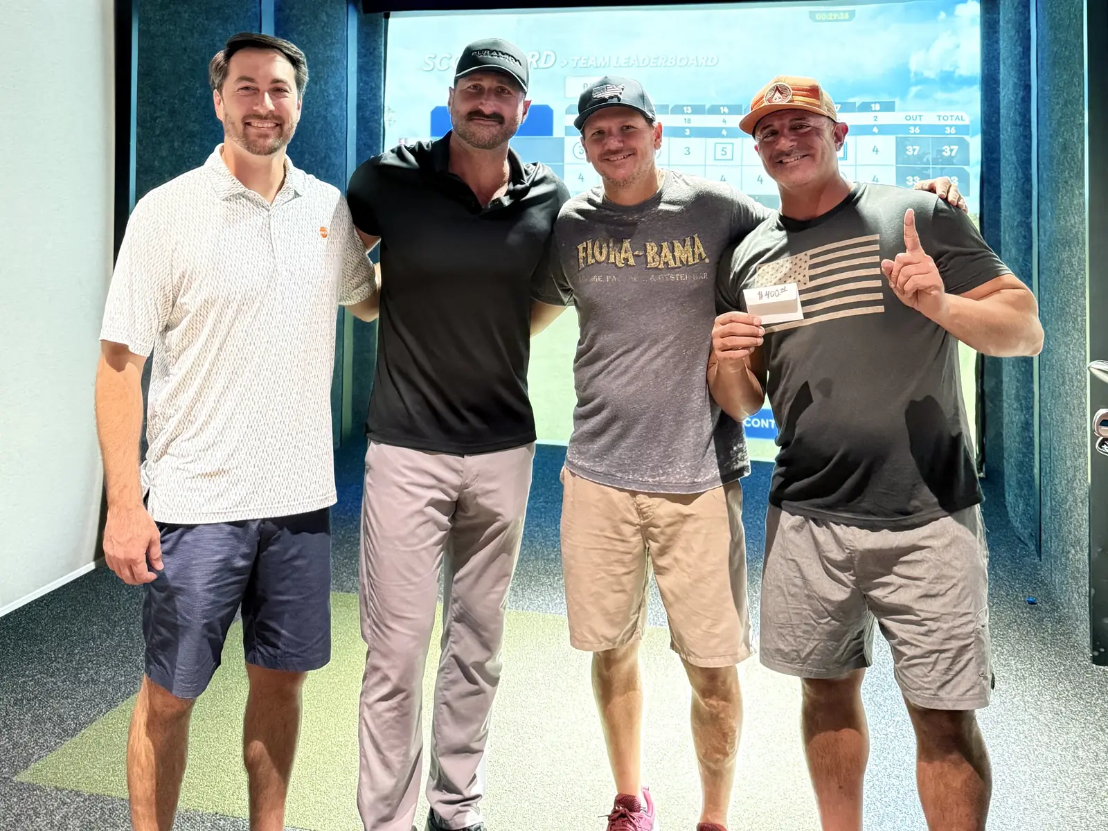 Four golfers in a simulator bay at Tee Off at The Wharf, facing the camera