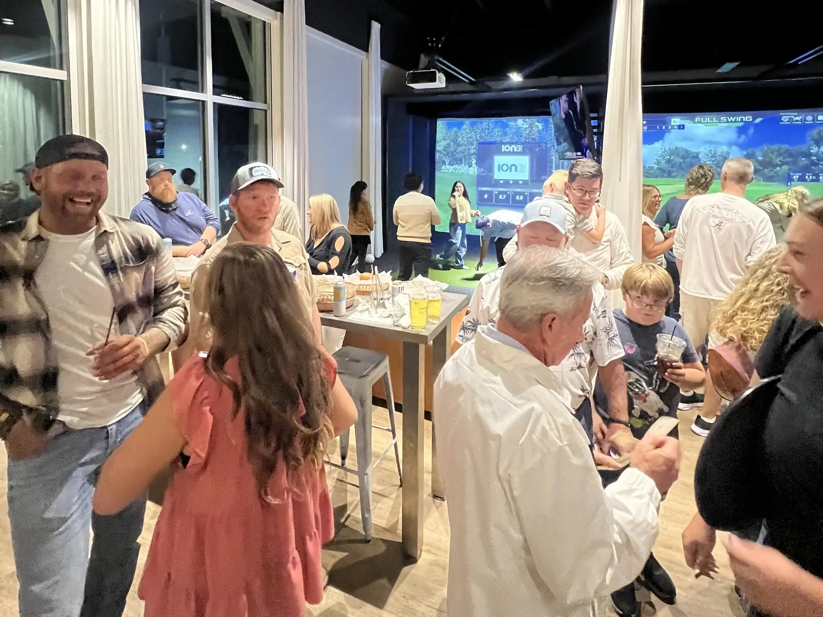 A party filling the room at Tee Off at The Wharf, guests around the high tables with the bays lit behind