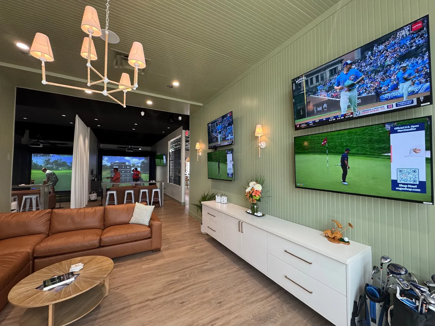 The lounge at Tee Off at The Wharf — live baseball and golf on the wall-mounted screens, with the simulator bays beyond