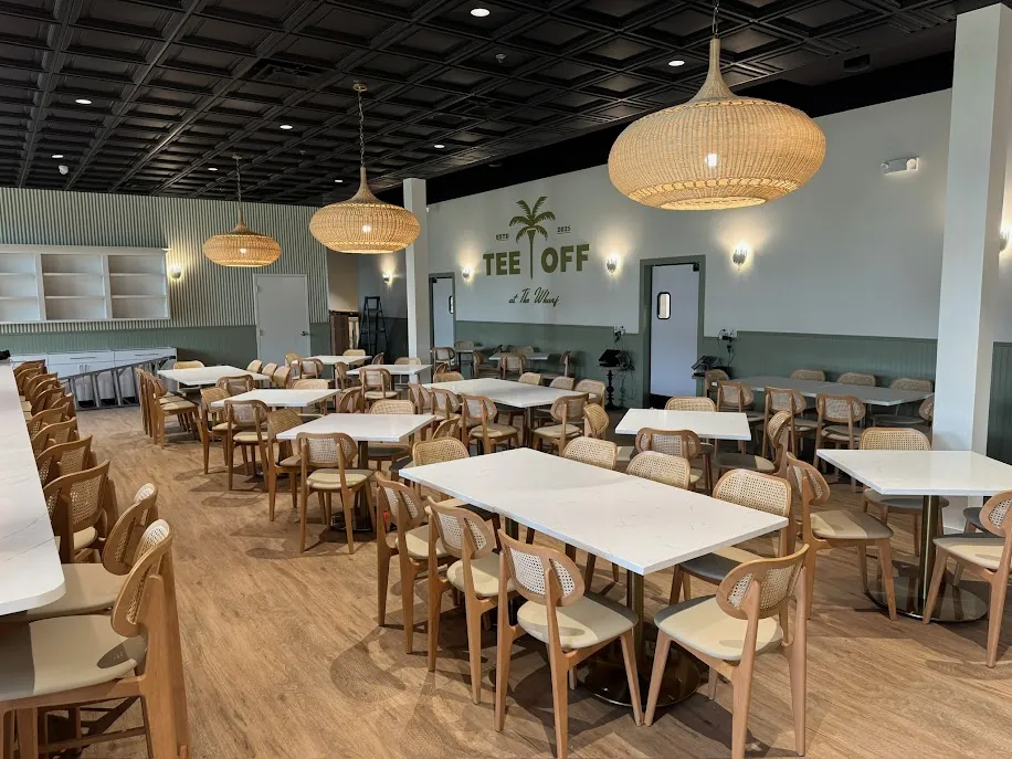 The dining room at Tee Off at The Wharf, with the palm mural and rattan pendants