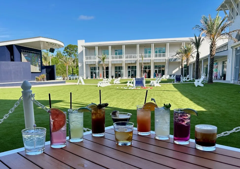 A row of ten cocktails on the patio rail, with the lawn at The Wharf behind