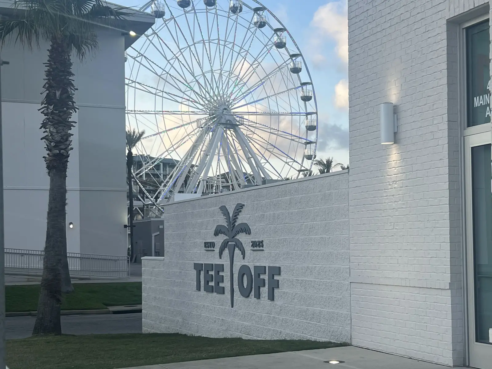 The Tee Off at The Wharf sign outside, with the Wharf ferris wheel rising behind it